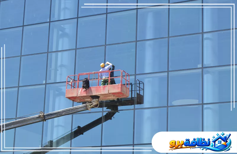 تنظيف الزجاج الخارجي للمباني بحفر الباطن 547528699 شركة نظافة برو عامل ينظف واجهة زجاجية لمبنى مرتفع باستخدام رافعة مخصصة لتنظيف الواجهات.